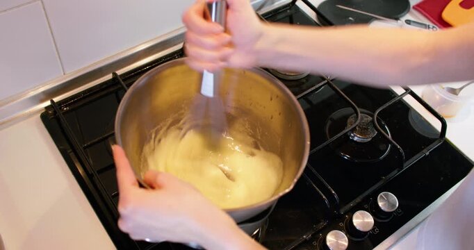 Food preparation. Whisking process. Chef hand stirring yellow liquid baking ingredient in stainless steel bowl with spring tool on stove.