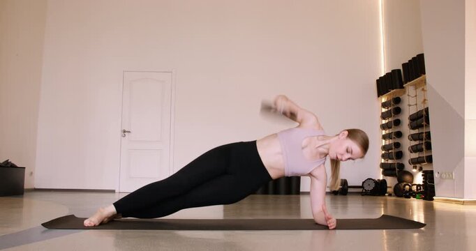 Plank exercise. Bodyweight training. Woman lifting heavy metal plate with core twist. Muscle strength workout in modern fitness studio.