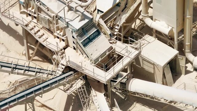 Heavy machinery transports limestone and aggregates through conveyor belts. Mining equipment operates in an open pit quarry. Industrial landscape showcases raw material processing.