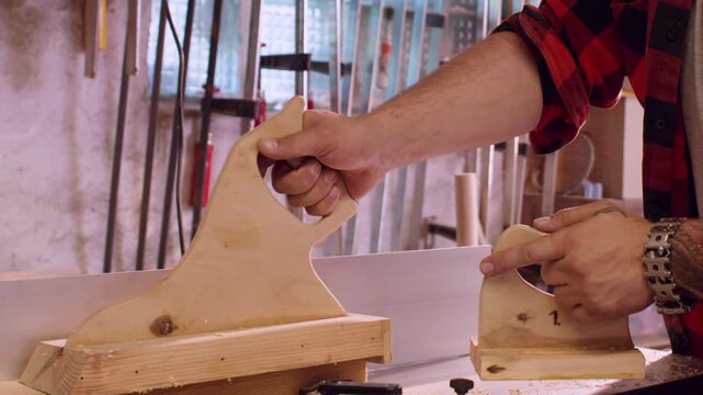 lumber service. Jointer machine. Male carpenter in red plaid shirt smoothing fresh cut plank on professional electric equipment with push block.