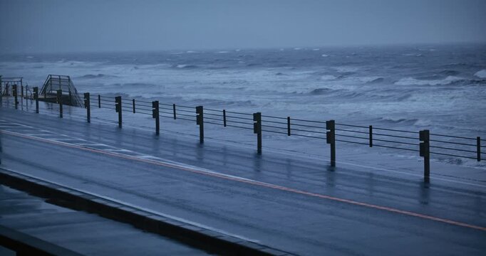 Van's driving down wet road near crashing ocean waves during storm - medium shot