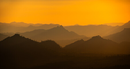 Fototapeta premium Stunning view of layered mountains and hills at sunrise. The golden morning light illuminates the silhouette of the land