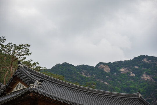 Traditional South Korea building roof with mountain and cloudy sky background.