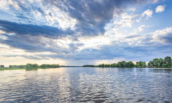 Wide river reflects sky's soft, dramatic clouds