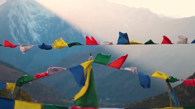 Landscape shot of colorful Buddhist prayer flags waving in front of snowy Himalayan mountain peak during the sunset as seen from Tayul Monastery near Keylong in Lahaul Valley, Himachal Pradesh, India.