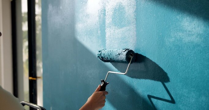 Painting, wall and hands of person with roller for home decoration, interior design and diy project. House, blue and painter with color, paintbrush and inspiration for remodeling, upgrade and change