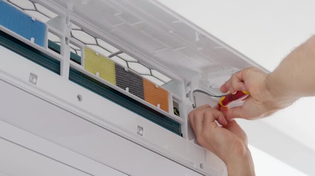 Hands repairing an open wall air conditioner with a screwdriver working near the filter and inner panel. Concept of AC repair and maintenance.