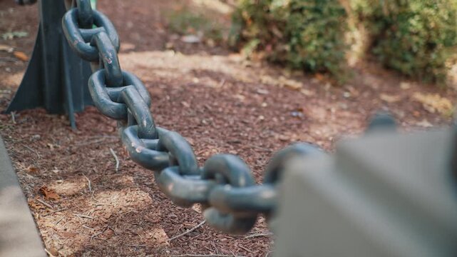 Close up metal chain with selective focus outdoors showing durable connected links against park ground and softly blurred surroundings