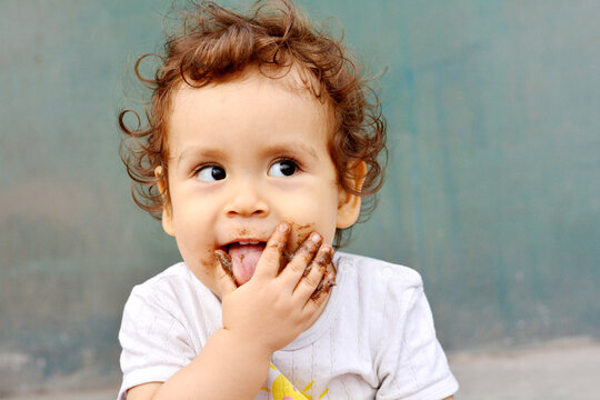 Smiling toddler. Hands and face in brown substance.
