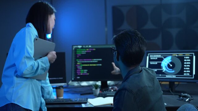 Asian female manager talking to male programmer writing code in dark blue office, Tech team discussing software development, cybersecurity and AI technology, Late night working business team concepts