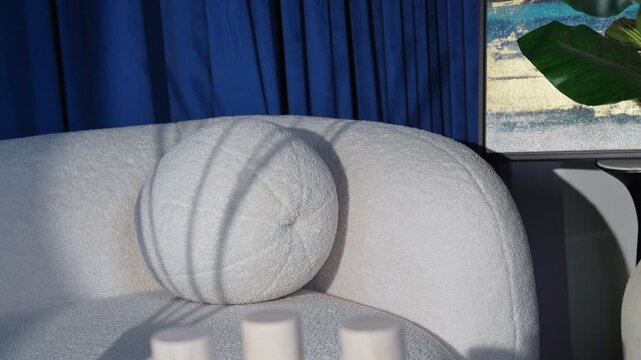 A cinematic shot of a luxury white boucl&eacute; sofa and ball pillow with dramatic window shadows, featuring deep blue velvet curtains and abstract art in a modern interior.