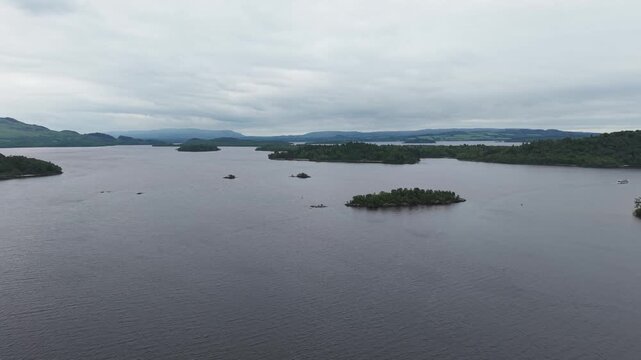 Scenic aerial view of islands on Loch Lomond near Luss. Beautiful aerial shot of calm lake water and green forested isles under overcast sky.