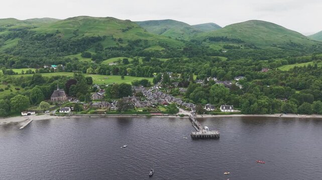 Scenic aerial view of beautiful Luss village at Loch Lomond. Aerial shot of the historic lakeside town with pier and church under overcast sky.