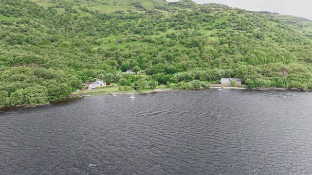 Scenic aerial view of Firkin Point shoreline at Loch Lomond, Scotland. Beautiful aerial shot of remote houses and lush green hills by the lake water.