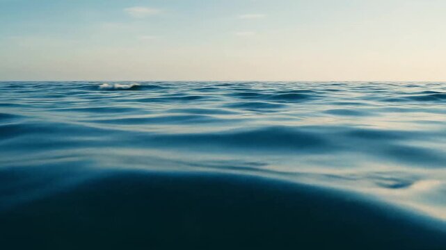 Calm ocean water with gentle waves under a clear sky, seen from sea level with a wide horizon and soft light.