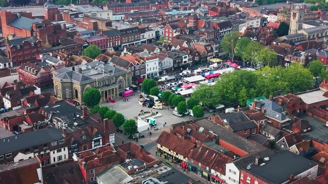 Drone footage looking across Salisbury Market Square with market stalls the Guildhall historic rooftops trees streets and St Thomas Church in the city centre.