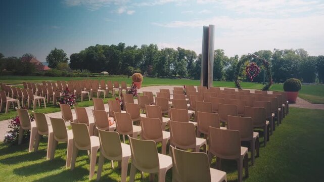Push in shot of empty wedding ceremony seats during the day with flowers and sun shining, outdoor, wide shot, gimbal