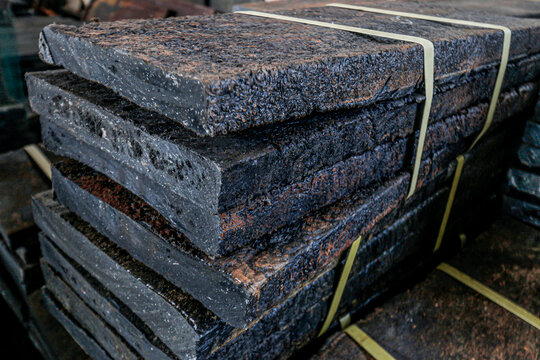 Recycled plastic waste is compressed into ecobricks. This photo shows an arrangement of rectangular, black-brown ecobricks with a rough, textured surface resembling melted plastic fibers.