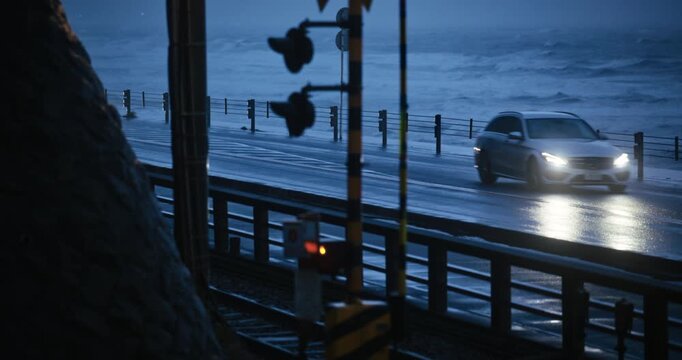Signal Light Foreground Cars Passing Wet Road With Nearby Rough Sea At Dusk