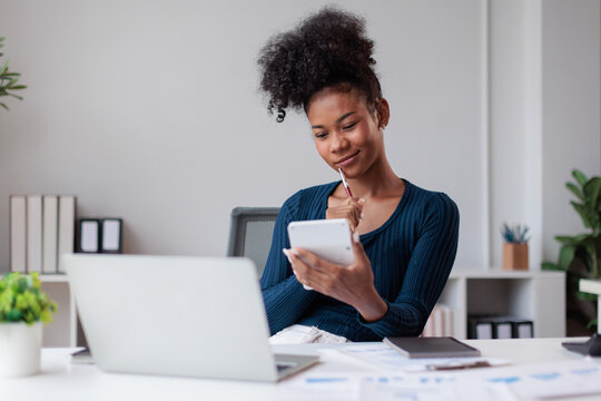 Young black businesswoman managing personal finances and business accounting, reviewing documents, using a calculator and laptop for financial planning and analysis