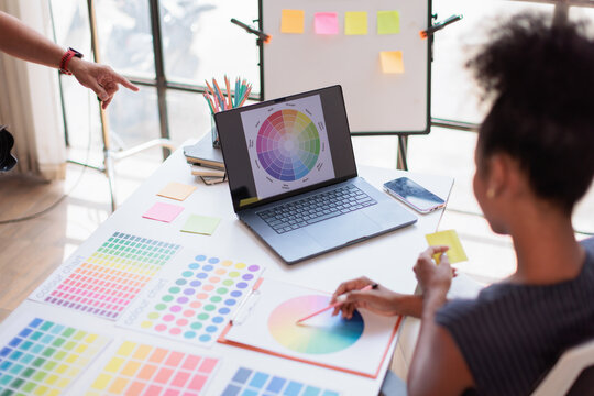 Designers collaborate at a modern studio, comparing a laptop color wheel with physical swatches to select brand colors while planning visual identity and creative strategy