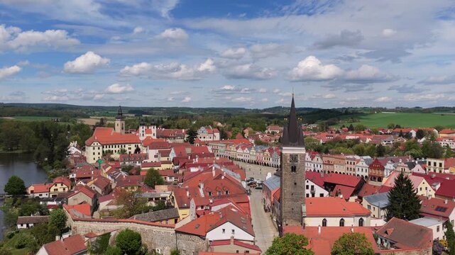 Aerial drone view of a Renaissance castle complex surrounded by ponds with a historic town square, church tower, and green countryside stretching to the horizon, Telc, Czech Republic
