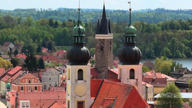 High-altitude aerial view of a historic Czech town with a colorful Renaissance square, castle, and twin ponds surrounded by rolling green farmland and forested hills, Telc, Czech Republic