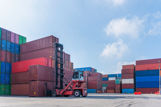 Heavy duty forklift lifting containers at global logistics distribution yard, Industrial reach stacker operating in container terminal, Cargo shipping containers stacked in rows at harbor