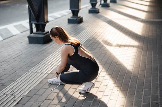 Woman in athletic wear crouching to tie shoelaces on a paved urban