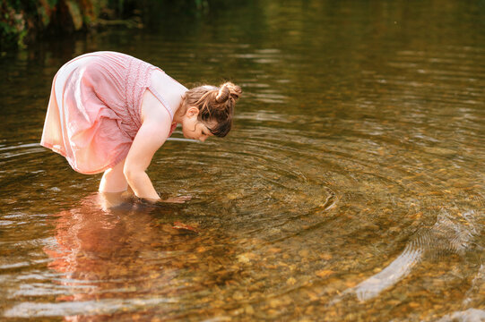 Young girl bending over to explore shallow stream water