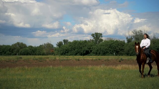 Woman riding a brown horse in a grassy field.