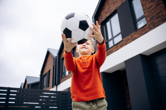 Boy catching soccer ball with both hands in a residential neighborhood, enjoying active playtime and childhood fun