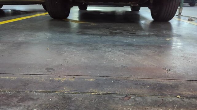 Close-up shot of a car tire slowly rotating backwards as the vehicle reverses into a parking space inside a shopping mall garage..