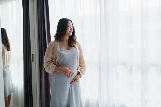 Young asian pregnant woman touching her belly at home