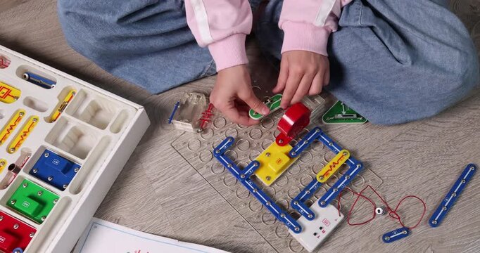 Child hands close-up turning switch on electronic circuit block constructor plate. Educational STEM activity for physics learning or engineering hobby promo. Real lifestyle physics experiment high
