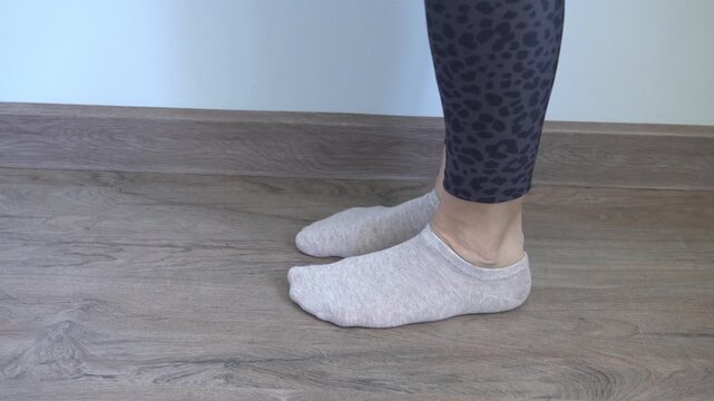 A woman is demonstrating a leg warm-up exercise before her workout. She is wearing socks and leggings, close-up shot.