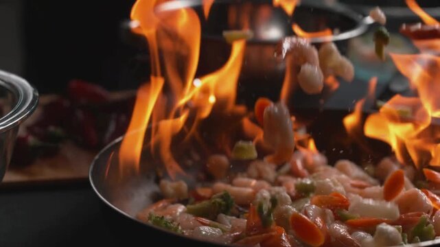 Chef stir frying shrimp and vegetables with large fire flames in wok, professional kitchen cooking with intense heat, cinematic flambe technique