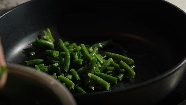 Green bean cooking. Hand puts green bean pods in a frying pan