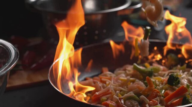 Flamb&eacute; cooking in professional wok pan, chef saut&eacute;ing fresh vegetables with fire flames, stir fry asian cuisine preparation in restaurant kitchen