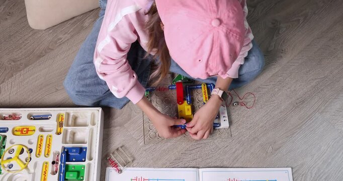 Girl wearing pink cap and smart watch connecting electronic circuit blocks to assemble radio transmitter. Educational STEM activity for physics learning or engineering hobby promo. Real lifestyle