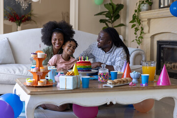 Obraz premium African American family leaning toward table in living room celebrating birthday with rainbow cake