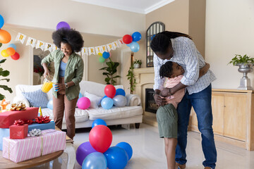 Obraz premium African American family celebrating birthday in living room with banner, woman pouring from pitcher