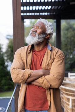 Senior African American man standing on deck under pergola, wearing rust T-shirt and tan shirt