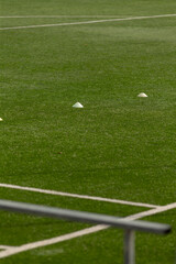 Obraz premium A close view of a green artificial turf sports field showing white training cones set along the grass near a marked sideline. Foreground features a blurred