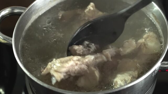 Making chicken broth. A person stirs chicken broth in a saucepan with a plastic spoon.