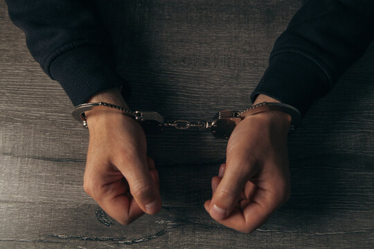 Hooded man in handcuffs on dark background. Criminal concept.
