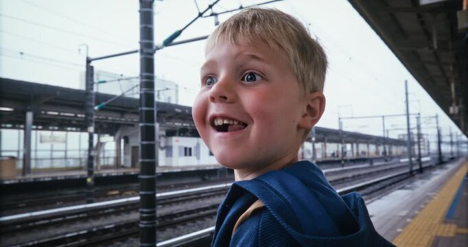 Happy little boy at Japanese train station looking up and down tracks - closeup