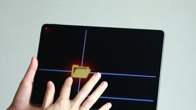 A hand is reaching out to a touchscreen showing file folders on a digital platform. The setting is indoors with a simple background. The person seems focused on their task.