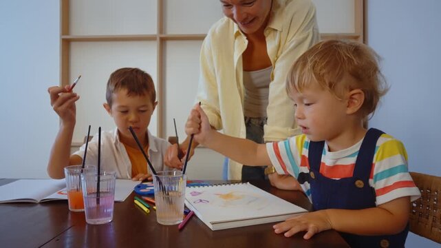 Young creative mother and her two little sons having fun painting with watercolors at home, engaging in a family artistic activity that promotes bonding and creativity for the children