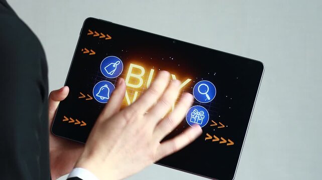 Person using tablet with buy now button displayed on the screen in a modern setting during daytime.